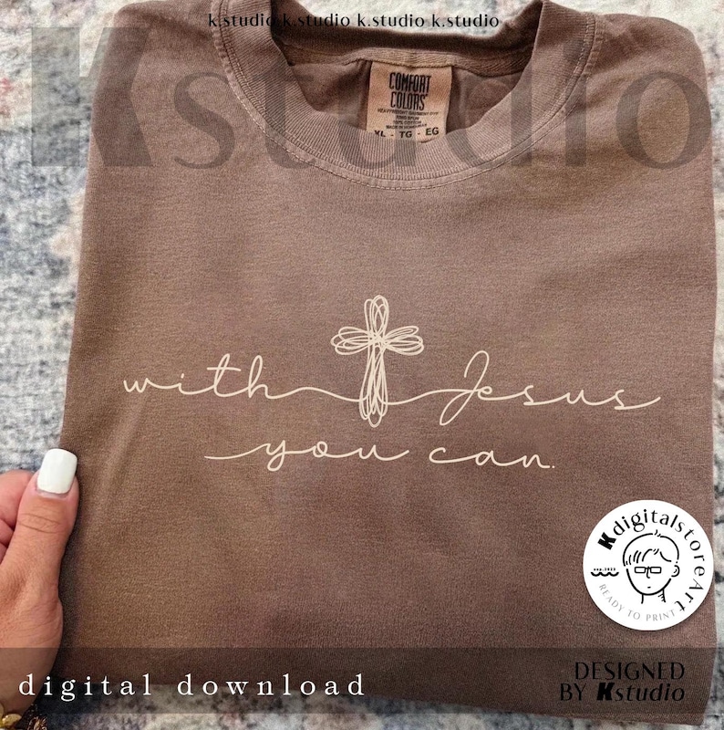 Op de afbeelding: Een bruin t-shirt met ronde hals, voorzien van een wit lijntekening-kruis en de cursieve tekst with Jesus you can. Het shirt heeft een Comfort Colors merklabel in de binnenhals met maat XL en een ronde sticker in de hoek van de afbeelding.