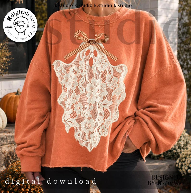 May include: An orange long-sleeve sweatshirt featuring a large white lace ghost graphic on the front. The ghost design is accented with a brown and white gingham patterned bow at the top. The sweatshirt has a crew neckline and a relaxed fit.