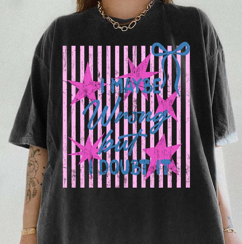 Może przedstawiać: Czarny t-shirt z r&oacute;żowo-białym wzorem w paski. Koszulka zawiera napis "I MAYBE WRONG BUT I DOUBT IT" w kolorze niebieskim, z r&oacute;żowymi gwiazdkami i niebieską kokardą.