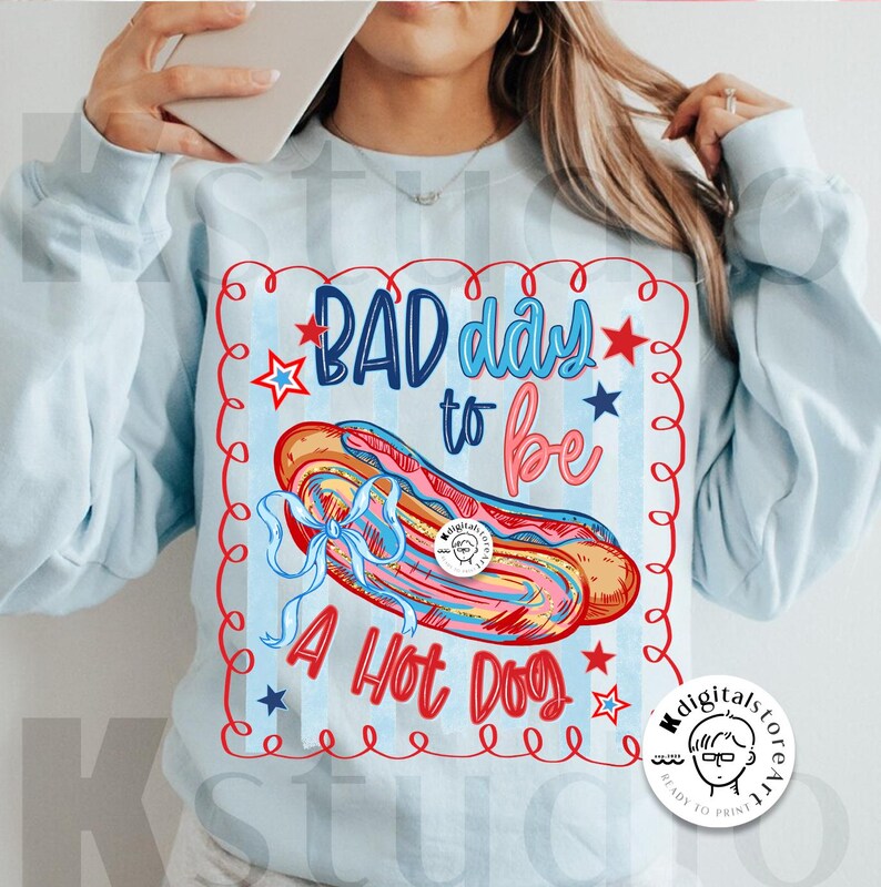 May include: Light blue sweatshirt with a graphic that says "BAD day to be A HOT DOG". The graphic features a colorful hot dog with a blue bow, red stars, and blue and red text.