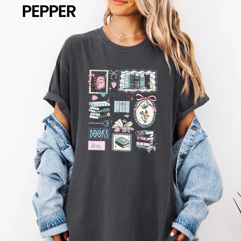 May include: Dark gray t-shirt with a colorful graphic of books, stamps, and floral elements. The word "BOOKS" is printed in a blue font, and the word "love" is printed in a pink font. The shirt has short sleeves.