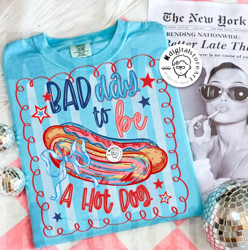 May include: Light blue t-shirt with a graphic of a hot dog and the text "BAD day to be A Hot Dog". The design includes red, white, and blue stars and stripes, and a blue bow.