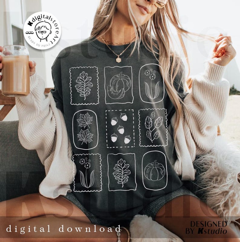 May include: Dark gray sweatshirt featuring nine white framed botanical illustrations, including leaves, pumpkins, and acorns. The words "digital download" are at the bottom. The design is by Kstudio.