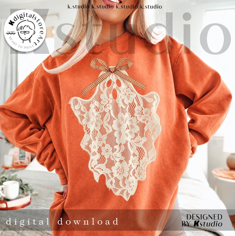 May include: An orange crewneck sweatshirt featuring a large, cream-colored lace ghost graphic on the front. The ghost design is adorned with a small, brown and white checkered bow at the top. The sweatshirt has long sleeves and a ribbed neckline.