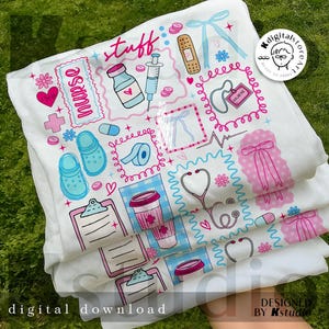 May include: White t-shirts with a colorful nurse-themed design. The design includes medical symbols, a stethoscope, a coffee cup, and the word "nurse". The shirts are stacked on top of each other.