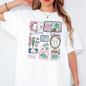 Op de afbeelding: Wit T-shirt met een kleurrijke collage van medische illustraties. Het ontwerp bevat postzegels met een spuit, stethoscoop, verband en een koffiekopje. Het woord "Nurse" is ook zichtbaar.