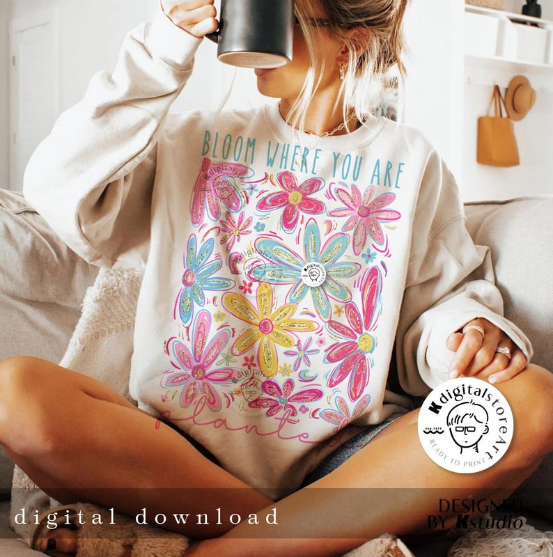 May include: A white sweatshirt with a floral design and the text "Bloom Where You Are" printed on the front. The flowers are in shades of pink, blue, yellow, and green.