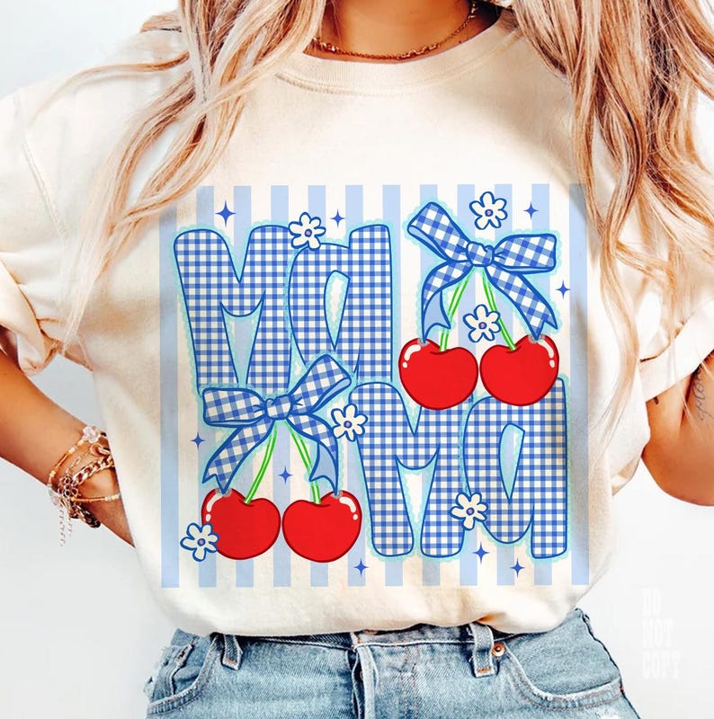 May include: Cream-colored t-shirt featuring the word "MOM" in a blue gingham pattern with red cherries and blue bows. The design includes white flowers and blue vertical stripes. A casual and cheerful design.