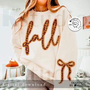 May include: Cream-colored sweatshirt with the word "fall" in a decorative, fall-themed font. A matching bow is on the sleeve. The design features orange, brown, and yellow floral patterns. The words "digital download" and "designed by Kstudio" are also visible.