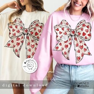 May include: Two women wearing pink and white sweatshirts with a large red and white heart-shaped bow design. The text "MdigitalstoreArt" is on the white sweatshirt. The text "DESIGNED BY Kstudio" is on the pink sweatshirt.