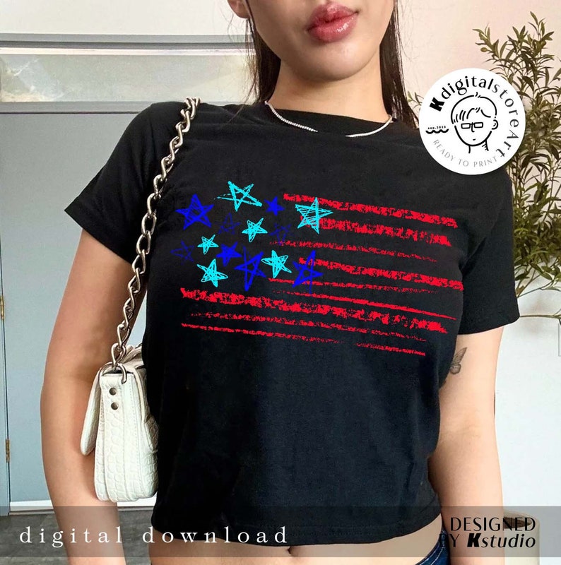 May include: A black t-shirt with a red, white, and blue American flag design. The stars on the flag are drawn in blue, turquoise, and black. The flag is distressed and has a grunge look. The t-shirt is a cropped style.