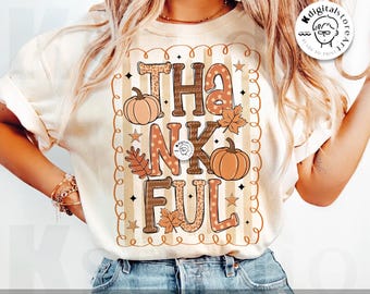 May include: Cream-colored t-shirt with the word "THANKFUL" in brown and orange letters, decorated with pumpkins, leaves, and stars. The shirt has a vertical striped background and a scalloped border. The words "digital download" are at the bottom.