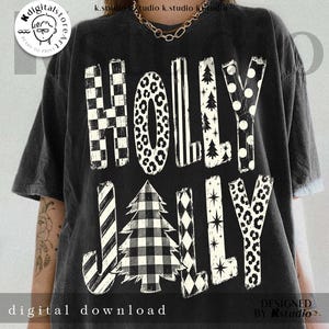 May include: A black short-sleeve t-shirt featuring the white text HOLLY JOLLY. The letters are filled with various patterns including checkerboard, leopard print, stripes, Christmas trees, polka dots, and stars, with a buffalo plaid tree.