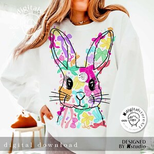 May include: A white sweatshirt with a colorful graphic of a bunny rabbit made of bows. The graphic is in shades of pink, blue, yellow, green, and purple. The text "Digitalstoreart" is on a circle in the bottom right corner of the image.