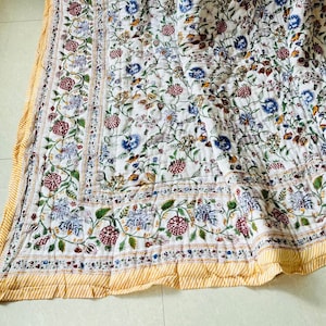 May include: A white cotton quilt with a floral print in shades of blue, red, and green. The quilt has a yellow border with a striped pattern.
