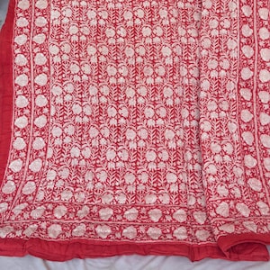 Puede incluir: Un edredón con estampado floral rojo y blanco. El edredón presenta un patrón repetitivo de flores y hojas blancas sobre un fondo rojo. El borde es de color rojo liso. El edredón está doblado sobre una superficie blanca.