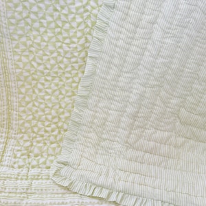 Könnte beinhalten: Ein gestepptes Textil mit einem hellgrün-weißen geometrischen Muster auf der einen Seite und einem hellgrün-weißen Streifenmuster auf der anderen. Das Stück ist mit einem Rüschenrand und dekorativen Ziernähten im Stoff versehen.