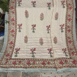 May include: Cream-colored quilt with a floral pattern in red and peach. The quilt features a detailed border with red roses and green leaves. The edges have a striped pattern in light blue and white.