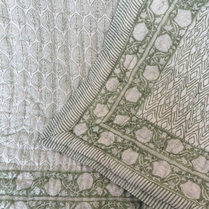 May include: A quilted textile featuring a white background with a repeating sage green leaf pattern. The border displays a sage green floral motif, a geometric diamond pattern, and thin striped edges, all stitched with visible quilting lines.