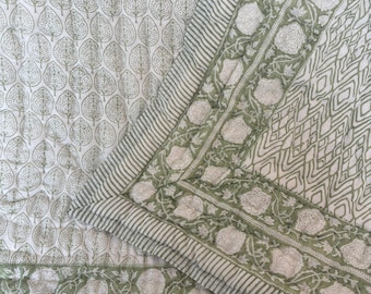 May include: A quilted textile featuring a white background with a repeating sage green leaf pattern. The border displays a sage green floral motif, a geometric diamond pattern, and thin striped edges, all stitched with visible quilting lines.