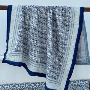 May include: A blue and white cotton quilt with a geometric pattern. The quilt has a dark blue border with a white and blue patterned trim.