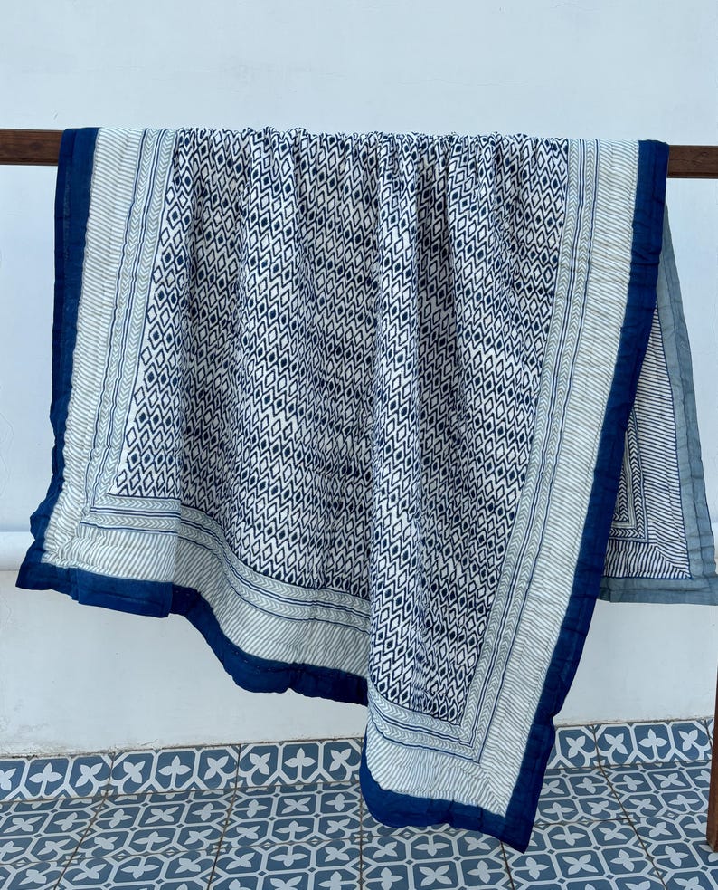 May include: A blue and white cotton quilt with a geometric pattern. The quilt has a dark blue border with a white and blue patterned trim.