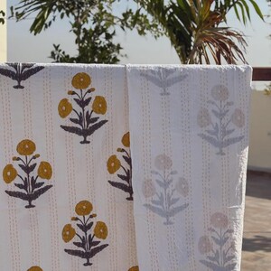 May include: A white cotton quilt featuring a repeating block-printed floral pattern in mustard yellow and dark gray. The fabric is detailed with vertical rows of fine, light-colored running stitches that create a textured, quilted appearance.