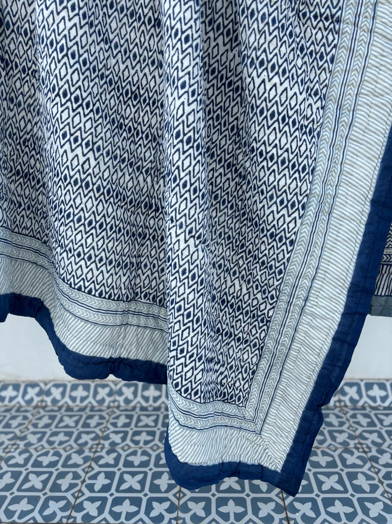 May include: A blue and white cotton quilt with a geometric pattern. The quilt has a blue border and is folded in half.