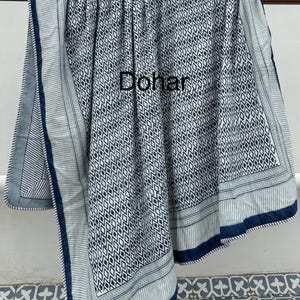 May include: A blue and white patterned cotton quilt with a geometric design. The quilt has a blue border with a white stripe and a green stripe. The word "Dohar" is written in black on the quilt.