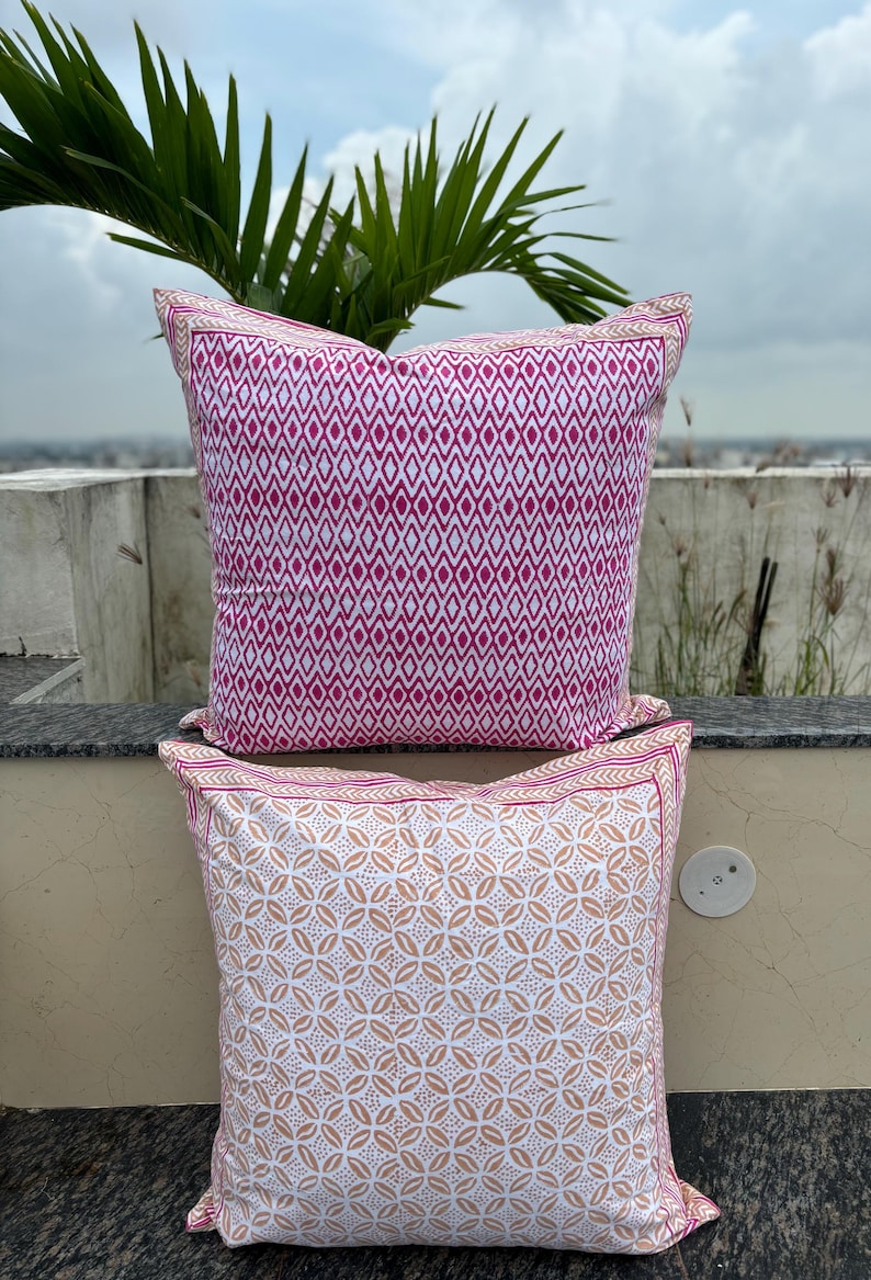 May include: Two square throw pillows with a white background and colorful geometric patterns. The top pillow has a pink diamond pattern and the bottom pillow has a light brown floral pattern.