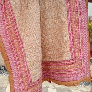 May include: A beige and pink cotton quilt with a floral pattern. The quilt has a border with a repeating pattern of pink and white stripes.