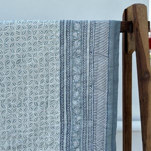 May include: A blue and white cotton quilt with a floral and geometric pattern. The quilt is hanging on a wooden rack.