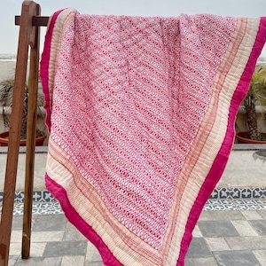 May include: A pink and white kantha quilt with a geometric pattern. The quilt has a cream border with gold embroidery and a pink border.