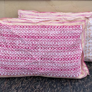 May include: Two pink and white patterned pillowcases with a geometric design. The pillowcases have a white background with a pink diamond pattern.
