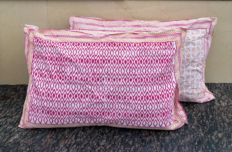 May include: Two pink and white patterned pillowcases with a geometric design. The pillowcases have a white background with a pink diamond pattern.