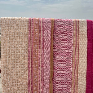 May include: A white cotton quilt with pink and brown printed patterns. The quilt has a geometric design with stripes and diamonds.