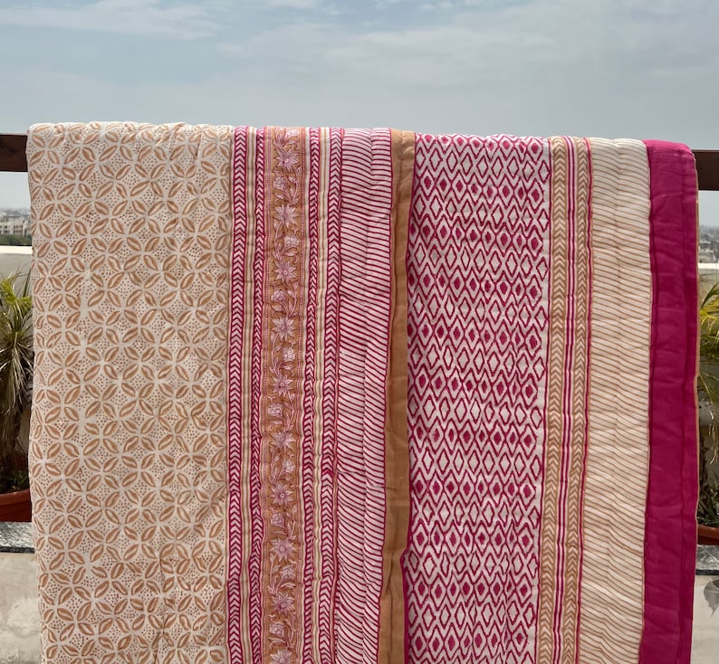 May include: A white cotton quilt with pink and brown printed patterns. The quilt has a geometric design with stripes and diamonds.