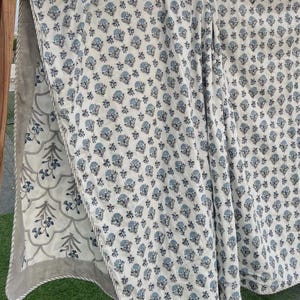 Può includere: Una trapunta reversibile caratterizzata da una base bianca con un motivo floreale blu ripetuto su un lato e una base bianca con un motivo botanico smerlato blu e grigio sul retro, rifinita con un bordo grigio e un profilo bianco.