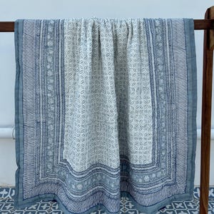 May include: A blue and white cotton quilt with a floral pattern. The quilt has a border with a geometric design.
