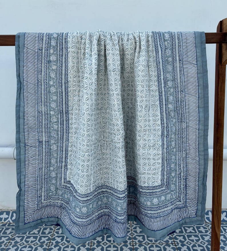 May include: A blue and white cotton quilt with a floral pattern. The quilt has a border with a geometric design.