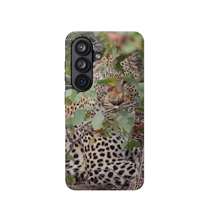 May include: A rectangular smartphone case featuring a high-resolution photographic print of a leopard partially obscured by green foliage. The case includes a vertical camera cutout on the upper left side with three circular black lenses visible.