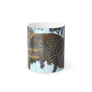 May include: A white ceramic mug featuring a photograph of a leopard resting on a tree branch. The text "Dreaming about that safari!" is printed in gold on the mug.