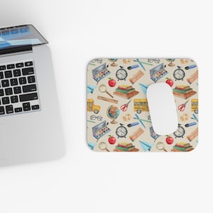 May include: A beige mouse pad with a repeating pattern of watercolor school supplies, including a school bus, globe, books, pencils, scissors, and paint palettes.