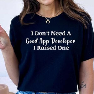 May include: Black t-shirt with white text that reads "I Don't Need A Good App Developer I Raised One"