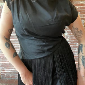 eye catching black 1960s dress with asymmetrical waistline and fringe skirt