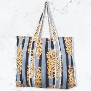 May include: A blue and black striped tote bag with a repeating pattern of yellow tigers. The bag has two long straps.