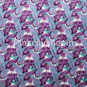 May include: A white fabric with a repeating pattern of purple and blue banana leaves. The leaves are stylized and have a graphic design.