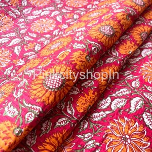 May include: A close-up of a pink fabric with a floral pattern. The fabric is covered in orange and white flowers with green leaves. The fabric is folded in half, and the flowers are visible on both sides.
