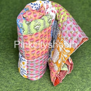 May include: A colorful patchwork quilt made of cotton fabric with floral and geometric patterns. The quilt is rolled up and has a red and white checkered border.