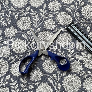 Op de afbeelding: Grijze stof met een witte bloemenprint. De stof wordt getoond met een schaar en een liniaal. De liniaal is gemarkeerd in inches.